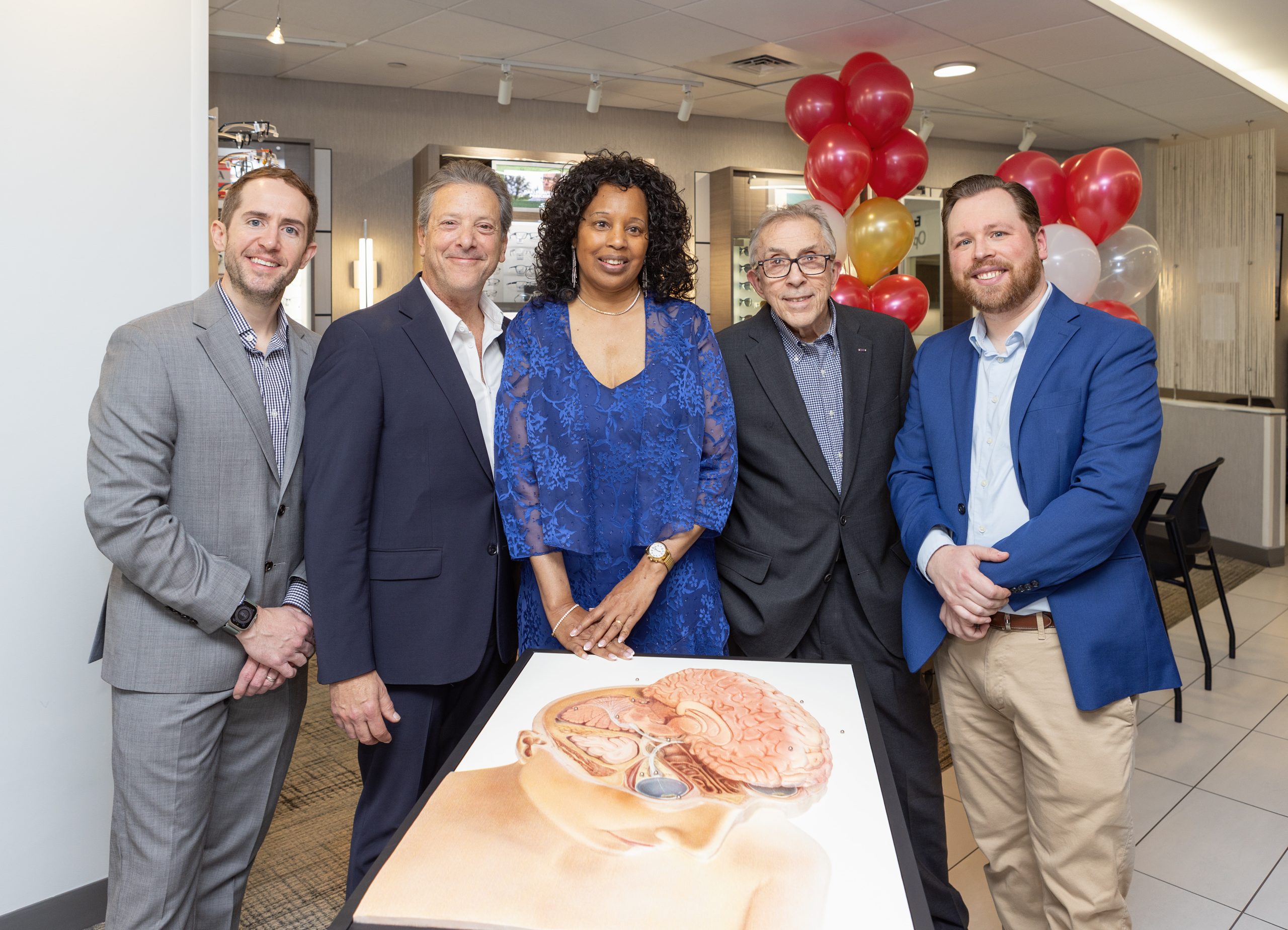 Janet LaBreck standing with group at New England College of Optometry. She's standing behind a tactile print of the human brain.